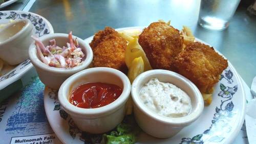 A plate of golden fried fish fillets with coleslaw, ketchup, and tartar sauce, garnished with lemon and lettuce.