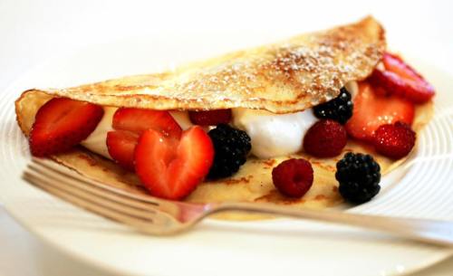 A delicious crepe filled with strawberries, raspberries, and blackberries, topped with cream, on a white plate.