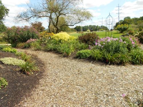 A scenic garden path surrounded by colorful flowers and greenery under a partly cloudy sky.