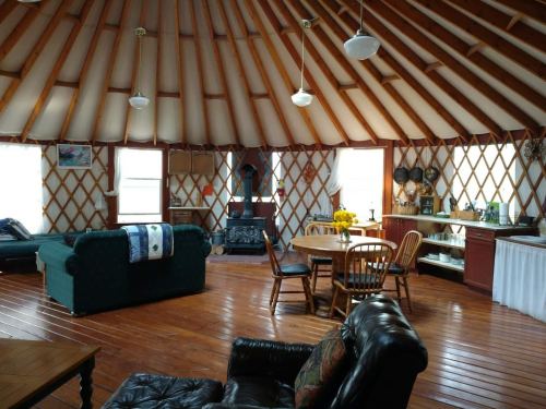 Cozy yurt interior with wooden floors, a round table, chairs, a couch, and a kitchenette, featuring a warm, inviting atmosphere.