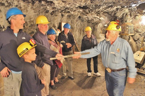 A group of people in hard hats inside a mine, watching a guide demonstrate with a tool.