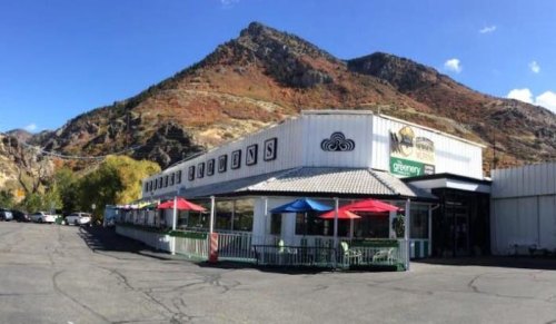 A restaurant with colorful umbrellas in front, set against a backdrop of mountains and a clear blue sky.