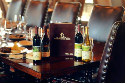 A dining table set with wine bottles, a menu, and plates, in a cozy restaurant setting.
