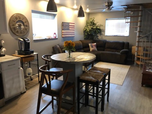 Cozy living space with a round table, chairs, a sofa, and decorative elements like plants and an American flag.