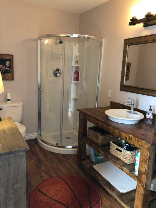 A modern bathroom featuring a glass shower, wooden sink stand, and rustic decor.