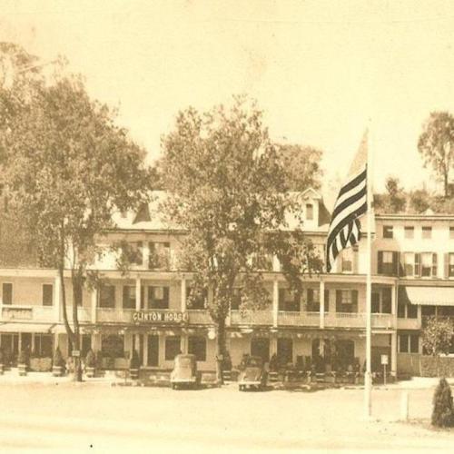 Historic photo of the Clinton House, featuring a flag and surrounding trees, with a vintage sepia tone.