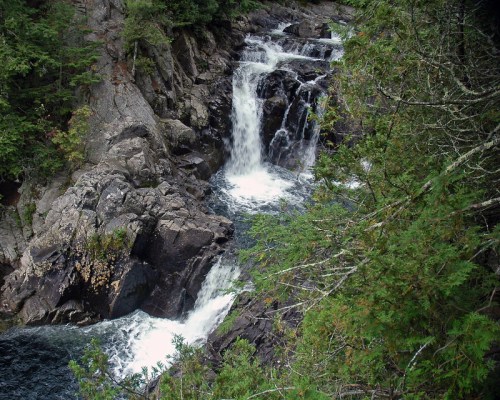 A serene waterfall cascading over rocky terrain, surrounded by lush greenery and trees.