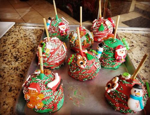 A tray of festive caramel apples decorated with green icing, sprinkles, and holiday-themed toppings.