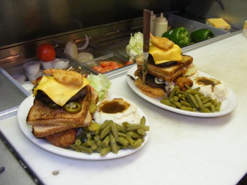 Two hearty plates of food featuring a stacked sandwich with cheese, fried onion, and sides of green beans and mashed potatoes.