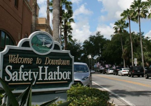 Sign welcoming visitors to Downtown Safety Harbor, lined with palm trees and a clear blue sky.