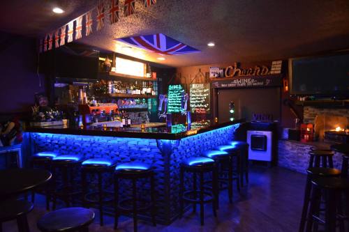 A cozy bar with a glowing blue counter, British flags, and a warm atmosphere, featuring stools and a fireplace.