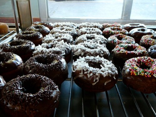 A variety of chocolate donuts topped with sprinkles, coconut, and chocolate sprinkles on a cooling rack.