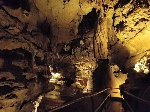 A dimly lit cave interior with rock formations and a winding pathway illuminated by soft lights.