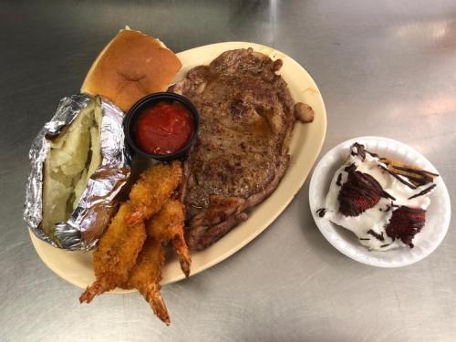 A plate with a steak, shrimp, baked potato, a roll, and a dessert of red velvet cake with cream and chocolate drizzle.