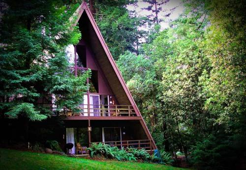 A triangular A-frame cabin nestled among lush green trees in a serene forest setting.