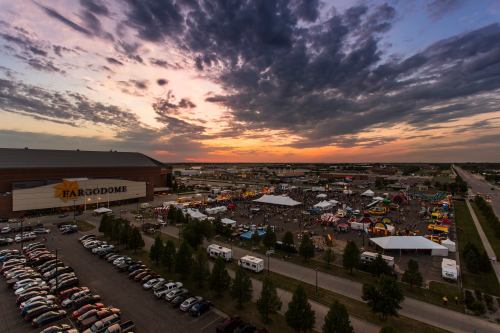 Aerial view of a lively outdoor event at the Fargodome, with colorful tents and a sunset sky.