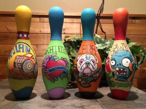 Four colorful bowling pins, each decorated with unique designs and names: Nolan, Katelyn, Laura, and Salvy.