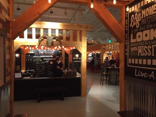 Interior of a rustic market with wooden beams, stalls, and warm lighting, featuring a bar and seating areas.