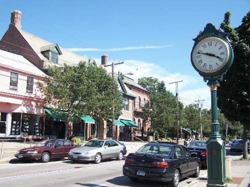 A street view featuring a clock tower, parked cars, and buildings with green awnings under a clear blue sky.