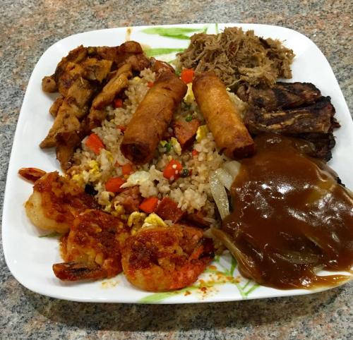 A plate of mixed Asian cuisine featuring fried rice, shrimp, chicken, spring rolls, and a savory sauce.
