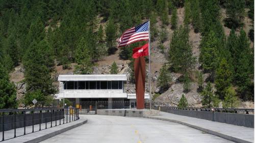 Entrance to a modern building with American and state flags, surrounded by trees and rocky terrain.