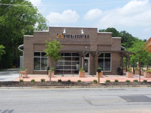 A modern brick building with large windows and a sign reading "Onarich," surrounded by greenery and a paved area.