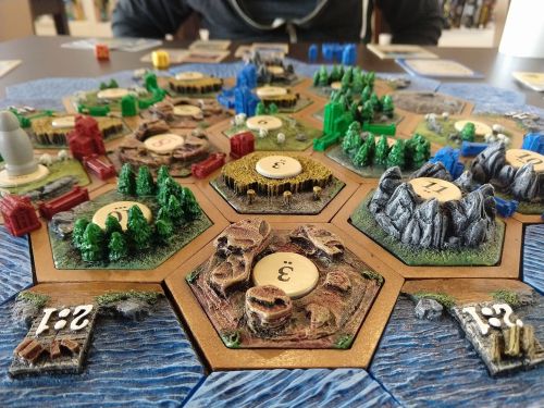 A colorful board game setup featuring hexagonal tiles with resources, settlements, and mountains, ready for play.