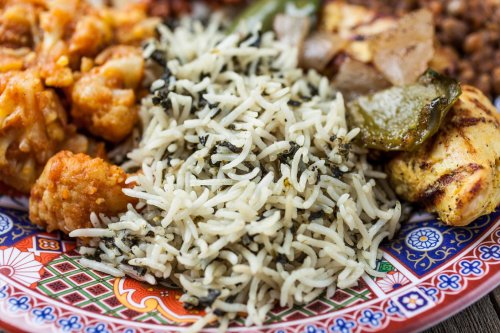 A colorful plate featuring rice with herbs, grilled vegetables, and various savory dishes.
