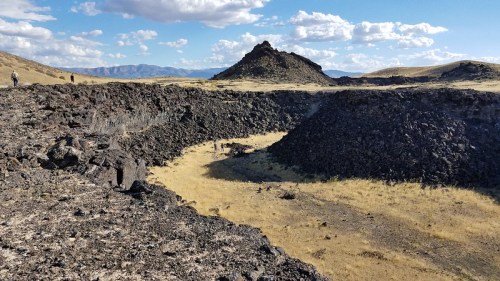 A rocky landscape with volcanic formations and sparse grass under a blue sky with scattered clouds.