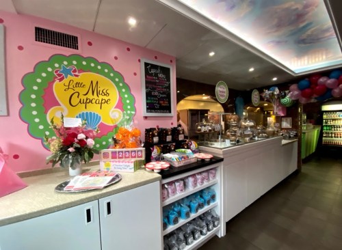 Brightly colored cupcake shop interior with a pink wall, display cases, and festive decorations.