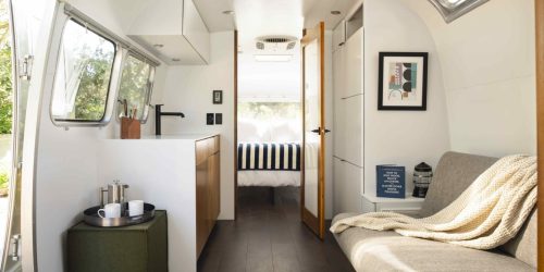 Cozy interior of a modern camper, featuring a kitchenette, seating area, and a bed visible through an open door.