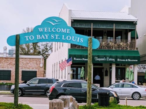 Sign welcoming visitors to Bay St. Louis, with a restaurant and American flag in the background.