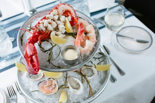 A seafood tower featuring lobster, shrimp, oysters, and lemon, served on ice with a side of dipping sauce.