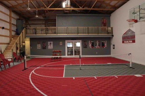 Indoor sports facility featuring a red and gray court, basketballs, and a balcony overlooking the playing area.