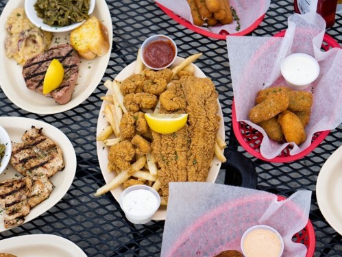 A spread of Southern dishes including fried fish, chicken, fries, and various dipping sauces on a picnic table.