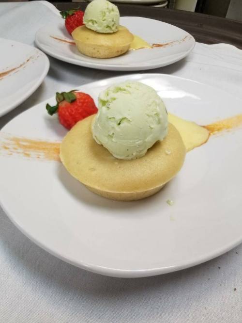 A dessert featuring a round cake topped with green ice cream, garnished with a strawberry and a drizzle of sauce.