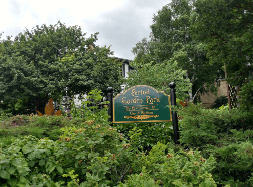 Sign for Period Garden Park surrounded by lush greenery and trees, with a cloudy sky in the background.