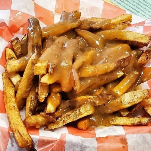 A basket of fries topped with brown gravy, served on a red and white checkered paper.