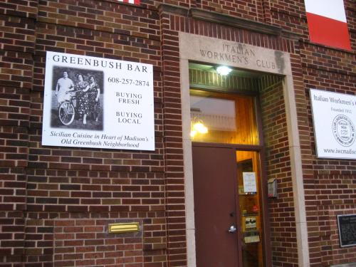 Entrance of the Italian Workmen's Club with signs for Greenbush Bar and local dining options. Brick facade visible.