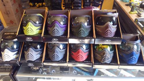 A display of various paintball masks in different colors, neatly arranged in their boxes on a store shelf.
