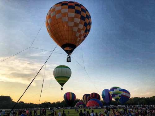 Colorful hot air balloons ascend against a sunset sky, with a crowd watching from below.