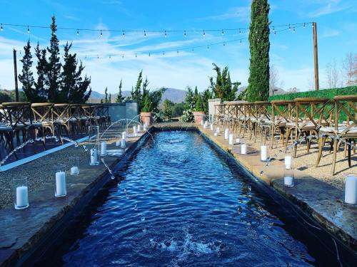 A serene outdoor venue featuring a water feature, lined with chairs and illuminated by string lights against a blue sky.