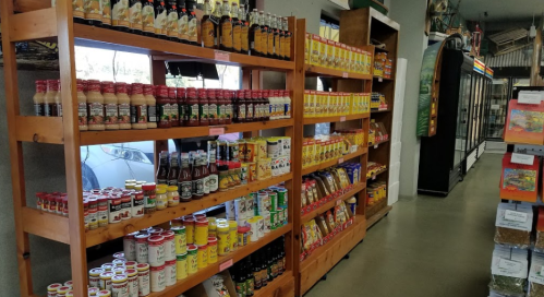 A grocery store aisle with wooden shelves filled with various jars, sauces, and packaged goods.