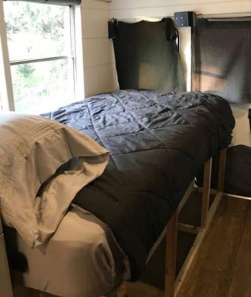 Cozy bedroom with a bed covered in a dark quilt, wooden frame, and natural light from a nearby window.
