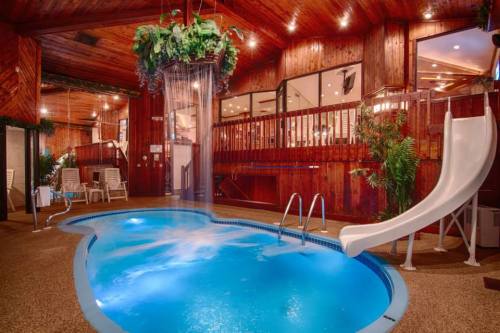 Indoor pool area featuring a slide, waterfall feature, and wooden decor with lush plants.