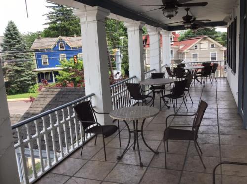 A covered porch with several tables and chairs, overlooking a street and colorful houses in the background.