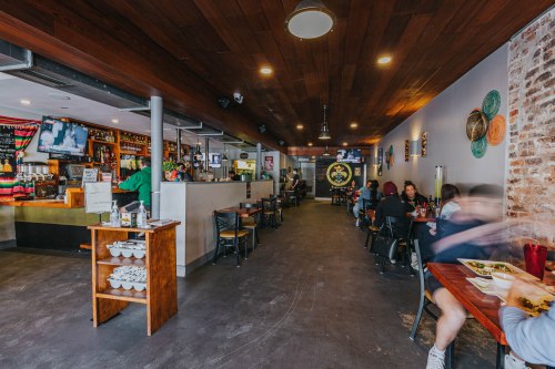 Interior of a lively restaurant with wooden accents, bar area, and patrons enjoying meals at tables.