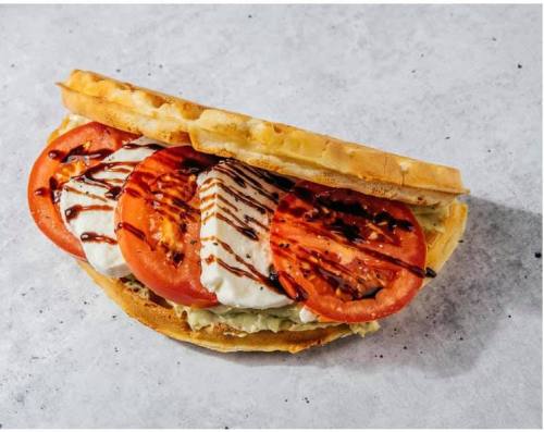 A waffle sandwich filled with sliced tomatoes, lettuce, and drizzled with balsamic glaze.