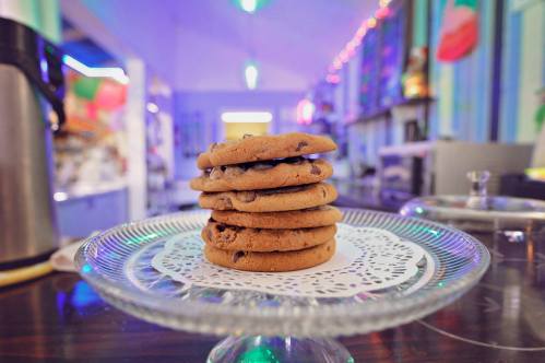 A stack of chocolate chip cookies on a decorative plate, set in a colorful, softly lit café.