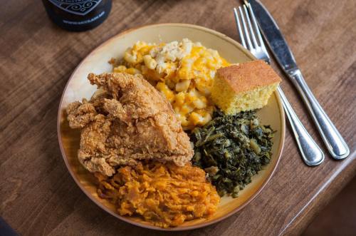 A plate of Southern comfort food featuring fried chicken, macaroni and cheese, cornbread, collard greens, and sweet potatoes.